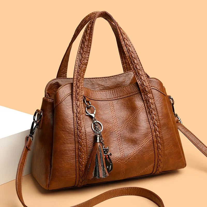 Brown leather shoulder bag with braided handle, zipper closure, and decorative tassel charm. Casual vintage style.