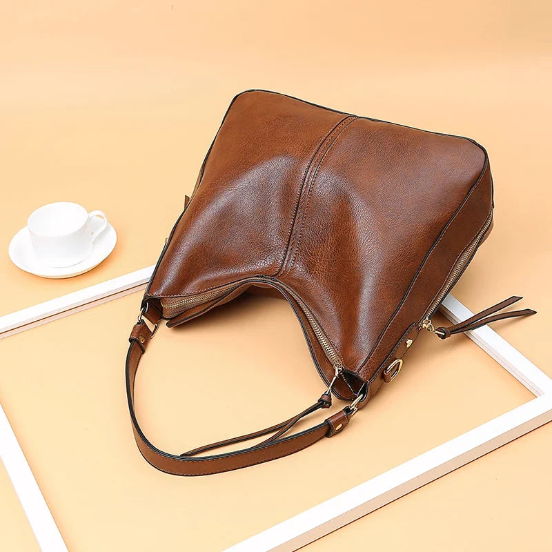 Large faux leather brown hobo handbag with a single shoulder strap and zipper closure, displayed on a soft beige background.