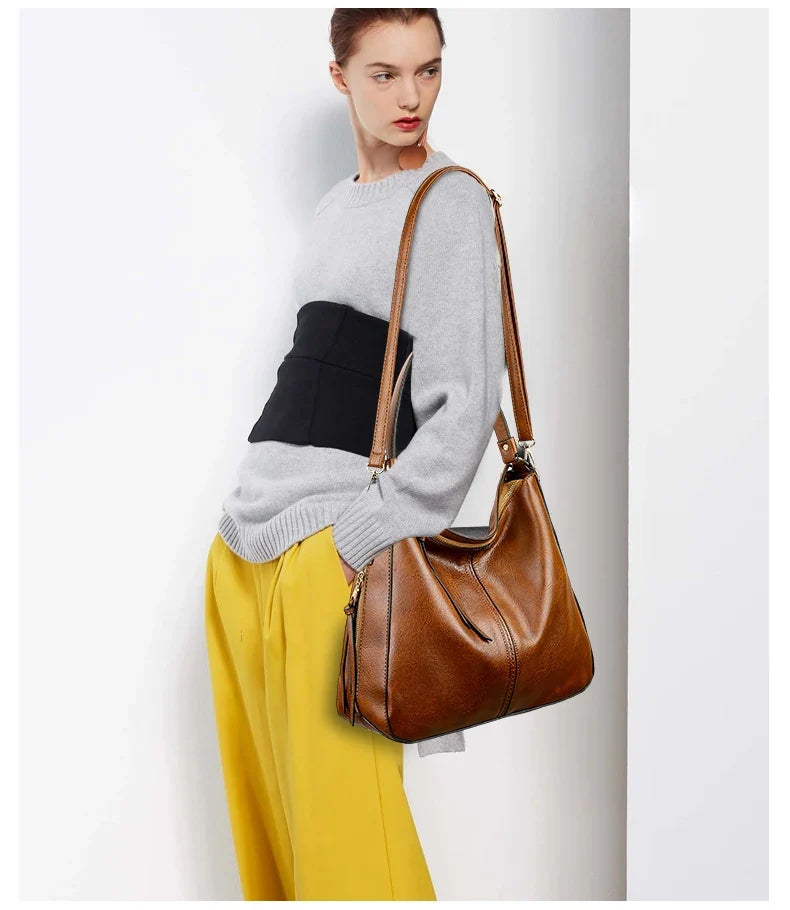 Brown faux leather hobo handbag worn on the shoulder, paired with a gray sweater and yellow trousers.