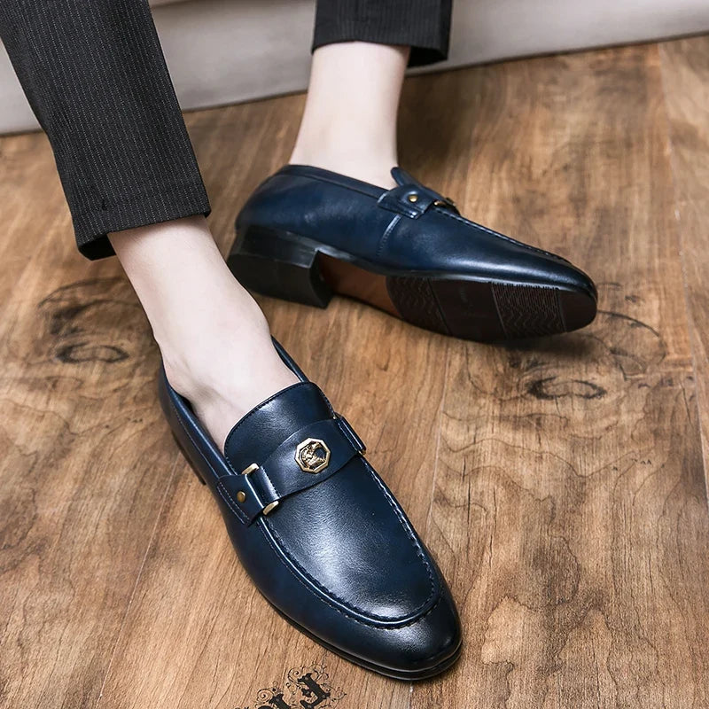 Men's navy leather loafers with a round toe and gold metal buckle, showcased against a wooden surface.