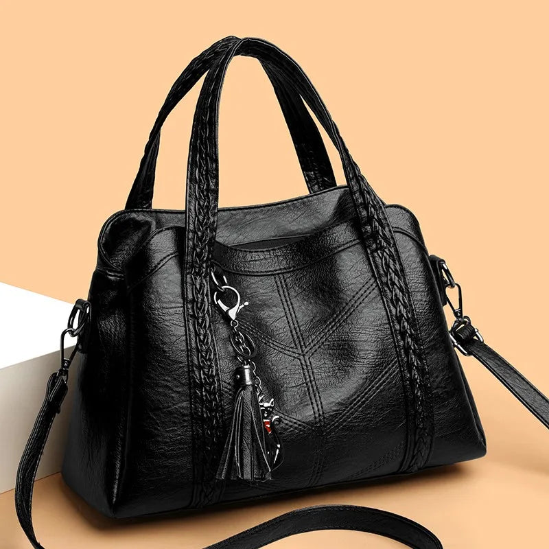 Black leather handbag with braided handles and a chic tassel charm, featuring a casual tote shape and zip closure.