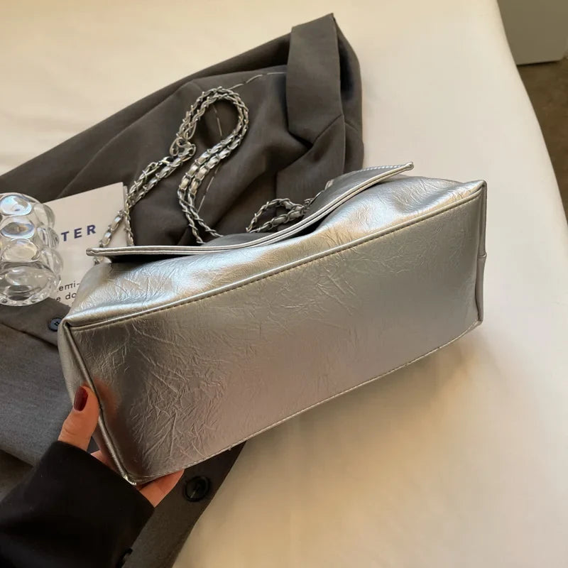 Silver shoulder handbag with a soft leather finish, two chain straps, and a casual tote shape.