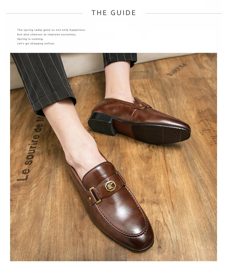Brown leather slip-on loafers with a round toe and a gold metal buckle detail, worn with pinstriped trousers.