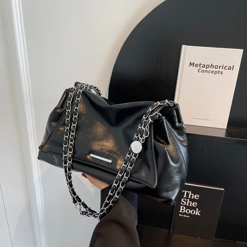 Black soft leather handbag with a chain strap, featuring a sleek design and a flap pocket.