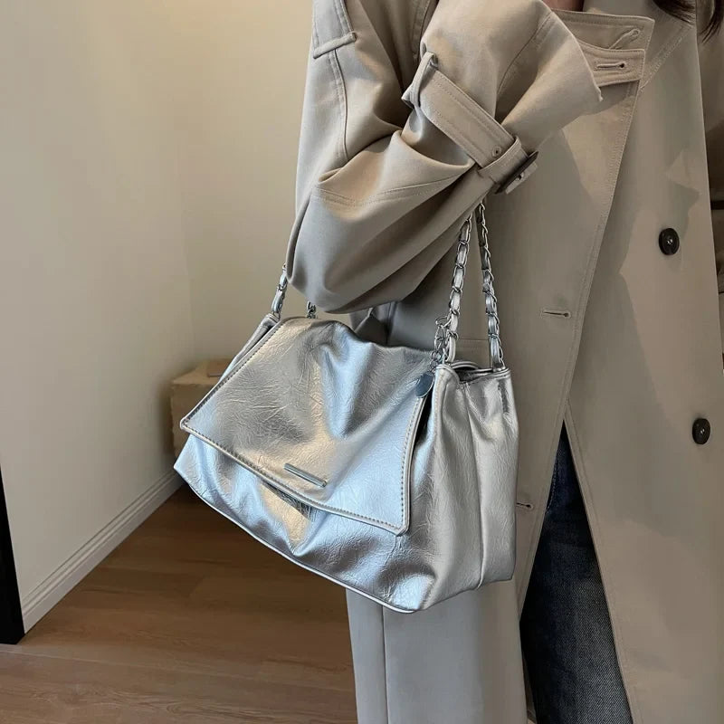 Silver shoulder bag with soft leather and a casual tote shape, held by a model wearing a light coat.
