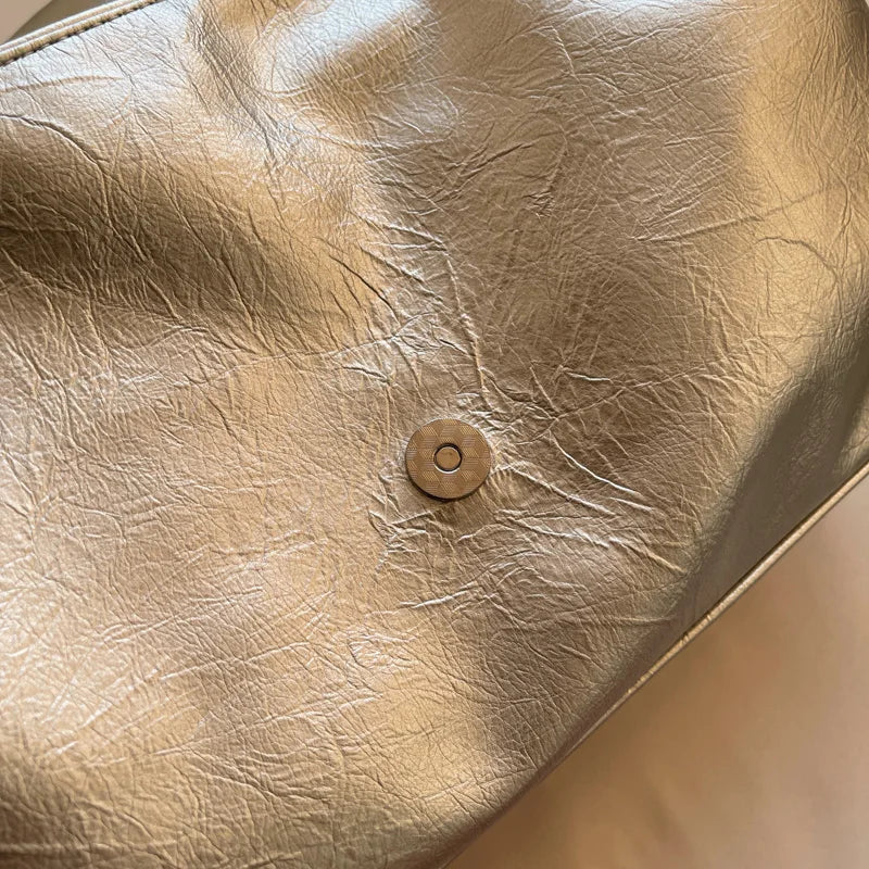 Silver soft leather shoulder bag showing a wrinkled texture and a circular snap closure, versatile for all seasons.