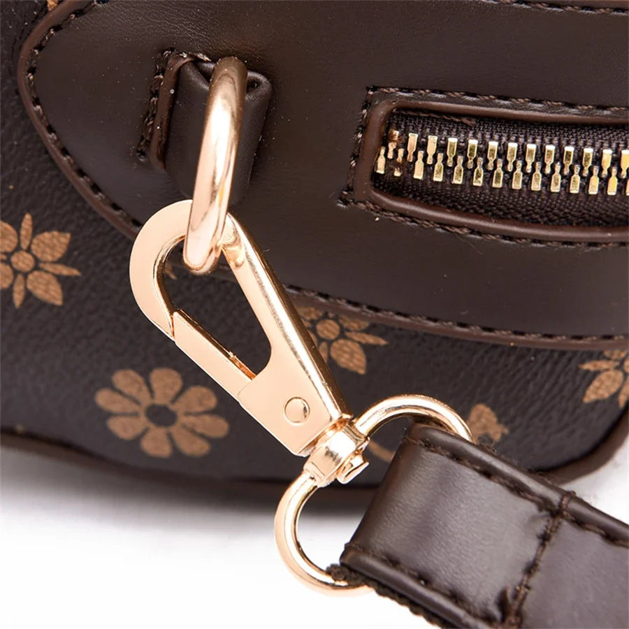 Gold clasp attachment on a dark brown handbag featuring a floral print and a zipper closure.