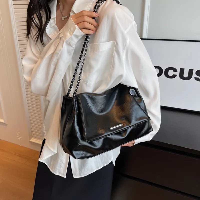 Soft black leather shoulder bag with a chunky chain strap, worn under the arm, featuring a flap pocket detail.
