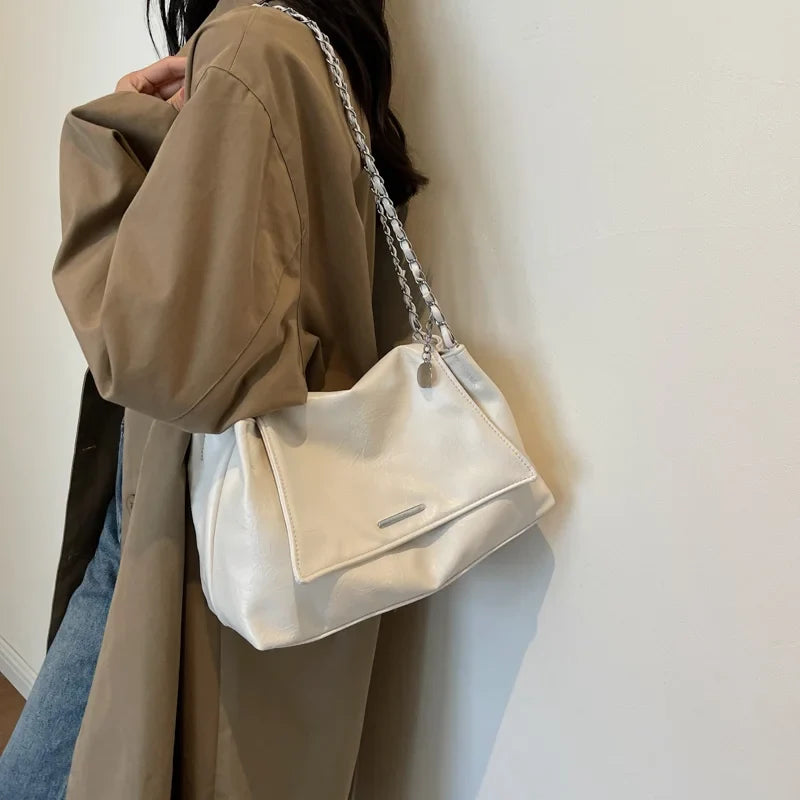Soft white leather shoulder bag with a chain strap, worn underarm, featuring a casual tote shape and flap pocket.