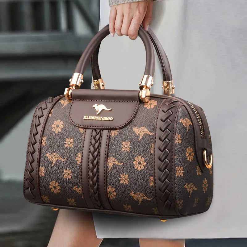 Brown handbag with gold floral patterns and kangaroo logo; features braided detailing and gold hardware.