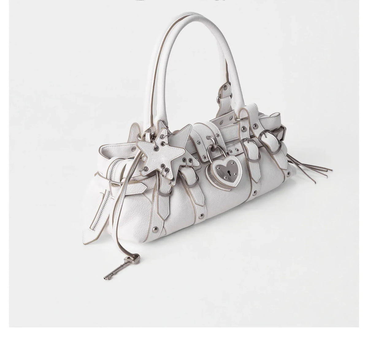 White handbag featuring silver rivets and decorative star and heart appliqués, styled as a casual crossbody.