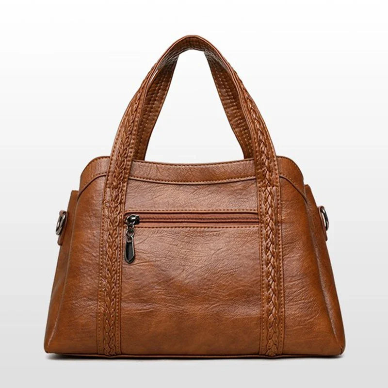 Brown leather tote bag featuring braided handles and a zipper pocket on the front, designed for casual use.
