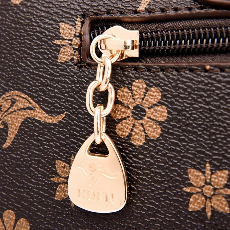 Brown handbag featuring a floral design, gold zipper pull, and a branded charm detail. Ideal for casual wear.