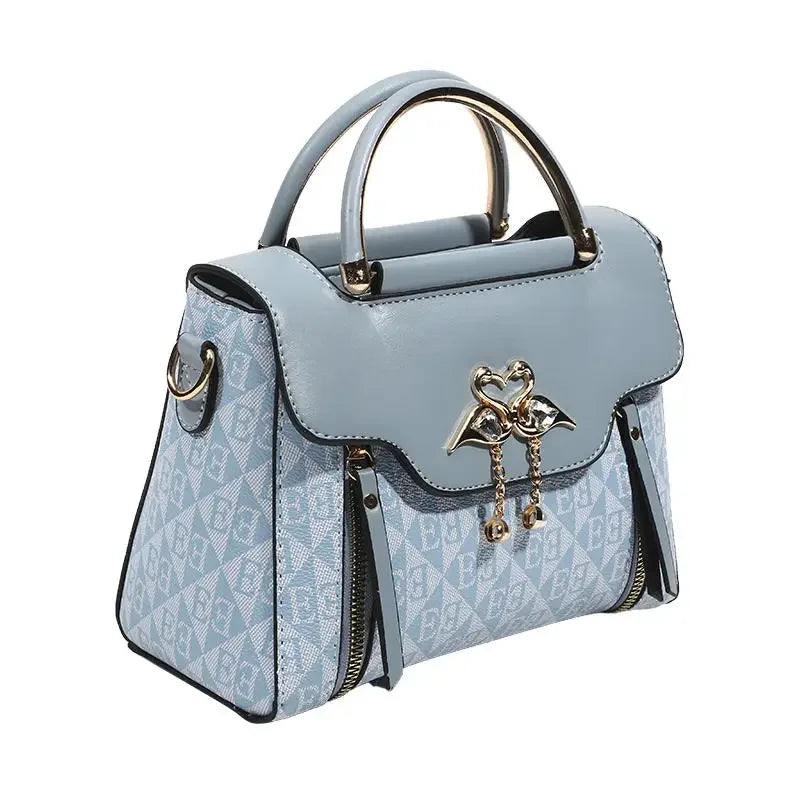 Light blue handbag with a structured shape, gold accents, and a distinctive heart pendant on the front.