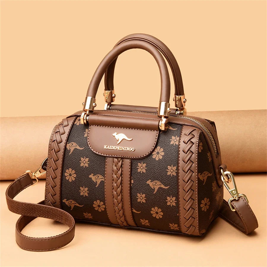 Brown luxury handbag featuring a semi-woven texture with floral and kangaroo patterns, dual top handles, and an adjustable shoulder strap.