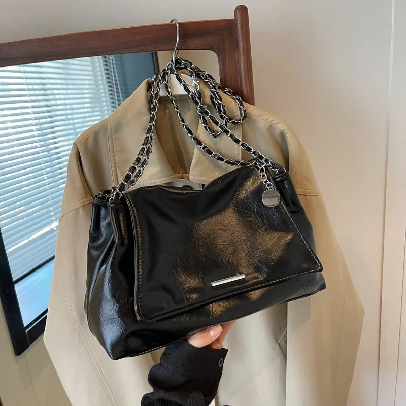 Black soft leather shoulder bag with a chain strap, featuring a flap pocket and silver hardware, held by a hand.