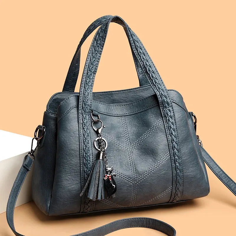 Soft gray leather handbag with braided handles and a decorative tassel charm, featuring a casual tote design.