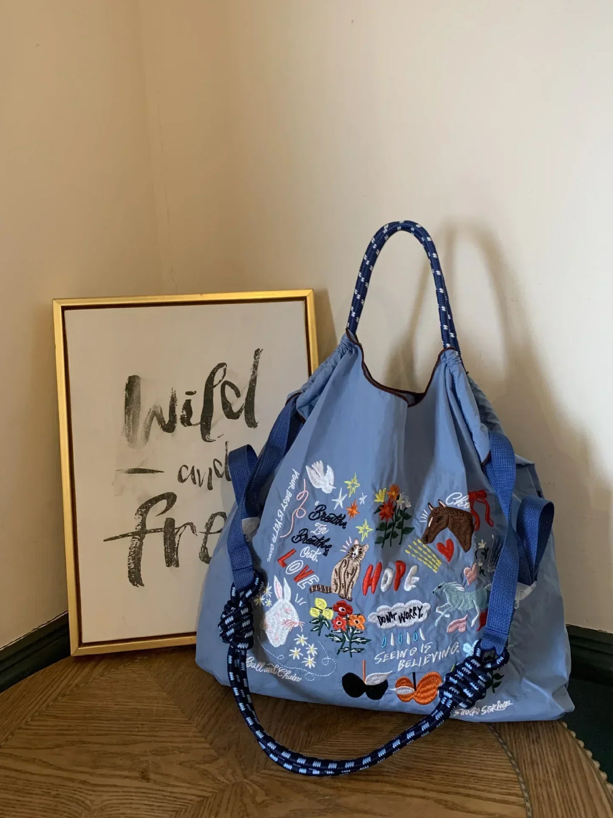 Light blue nylon tote bag with colorful embroidery and dual handles, suitable for casual or shopping use.