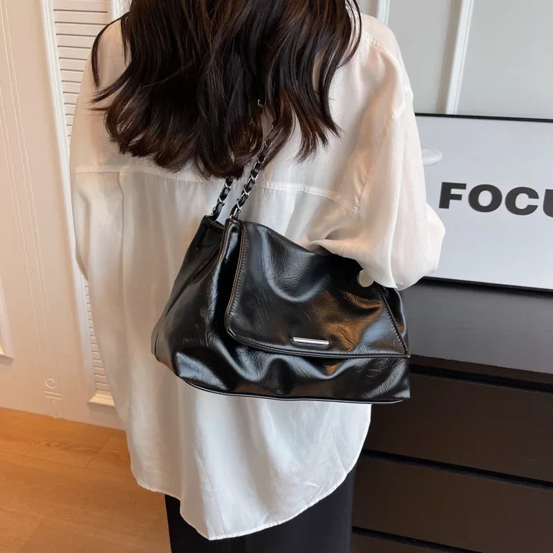 Large-capacity silver shoulder bag in soft black leather, worn underarm with a chain strap, styled with a white shirt.