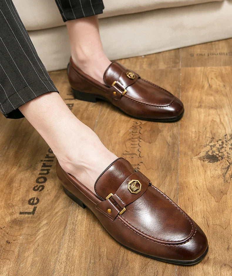 Brown leather loafers with a round toe, slip-on design, and a metal buckle detail, paired with striped trousers.