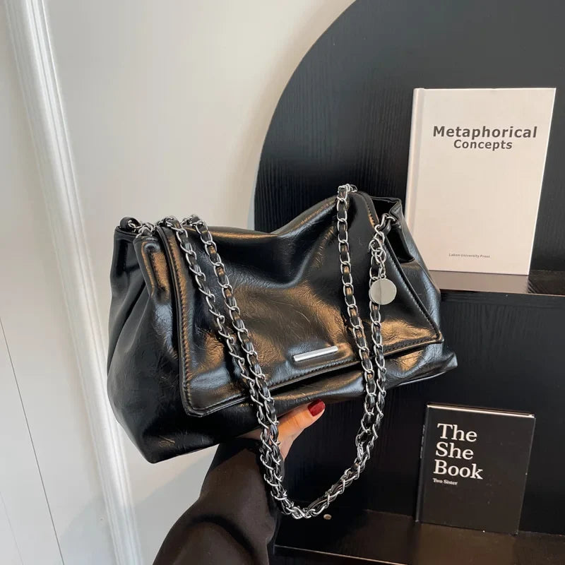 Black soft leather shoulder bag with silver chain straps, featuring a casual tote design and a flap pocket.