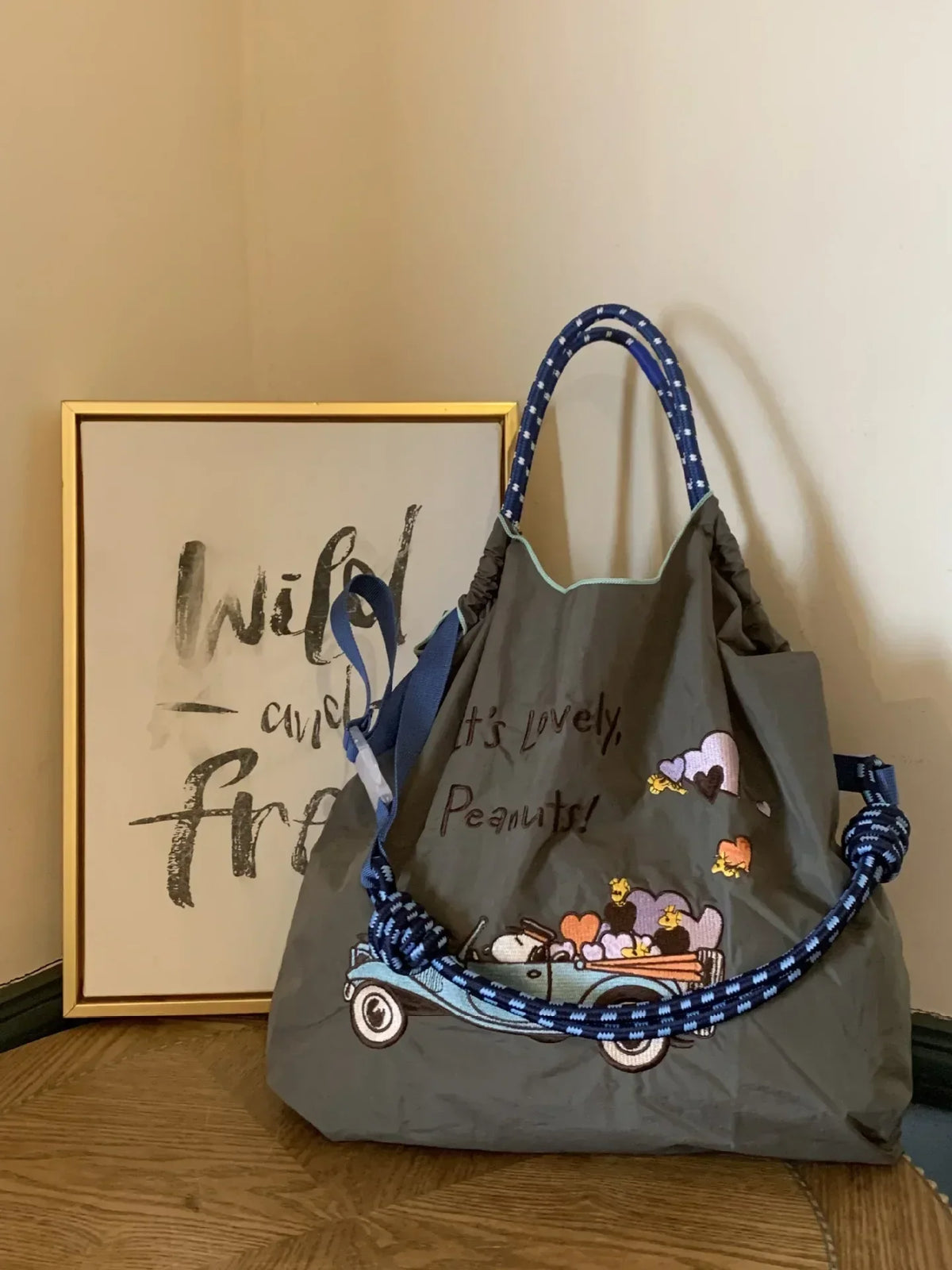 Large gray nylon tote bag featuring colorful embroidered design with a truck and hearts; stylish blue patterned handles.