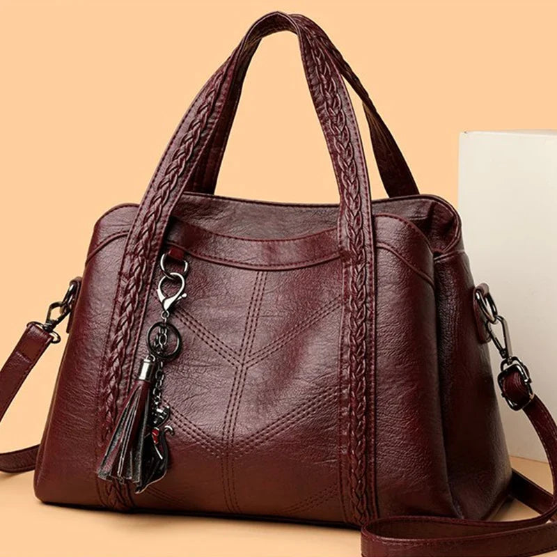 Burgundy leather handbag with braided handles and a detachable tassel, featuring a solid casual design and zipper closure.