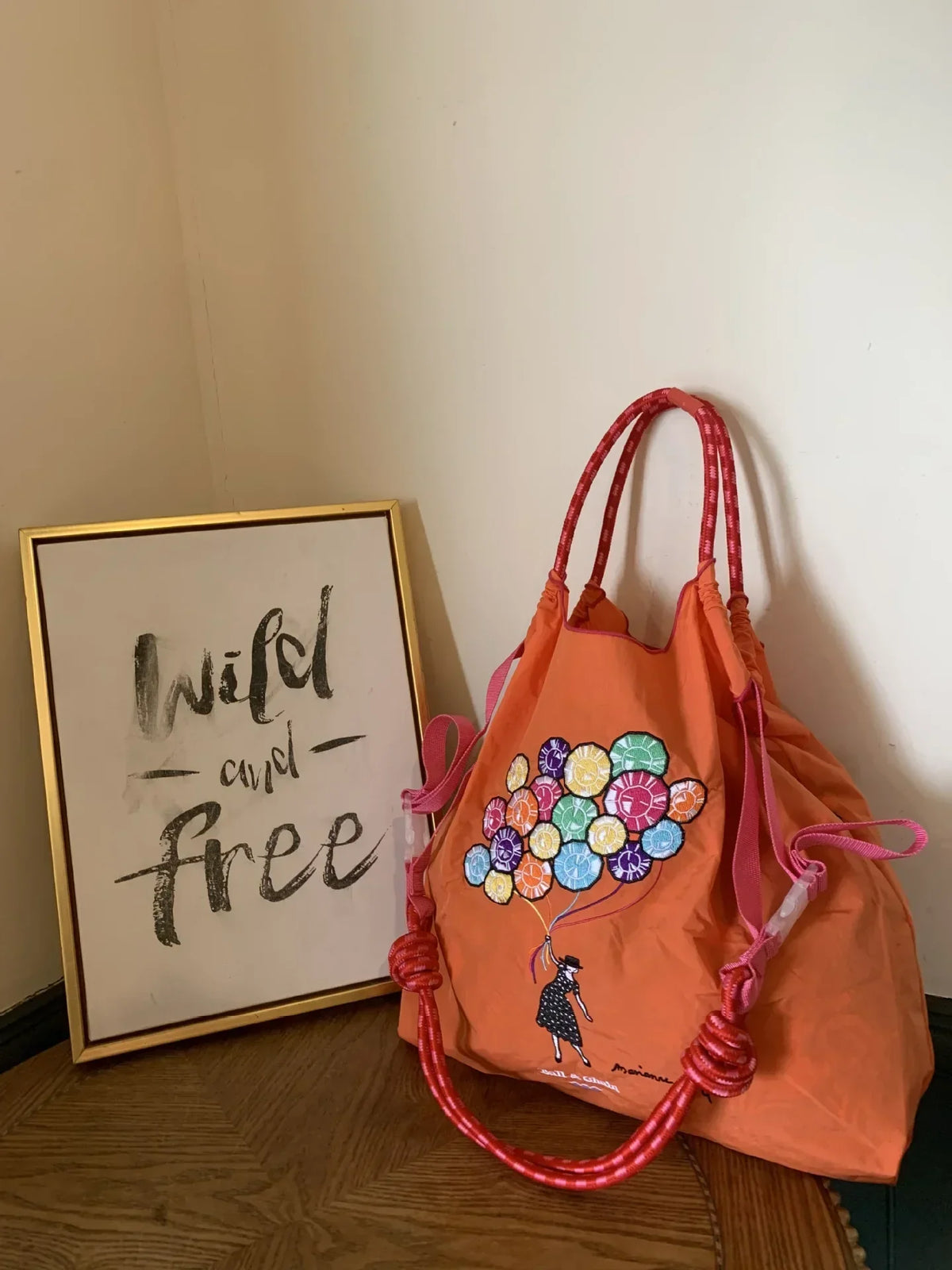 Large orange nylon tote bag with embroidered balloon design, pink handles, and a casual, foldable style.