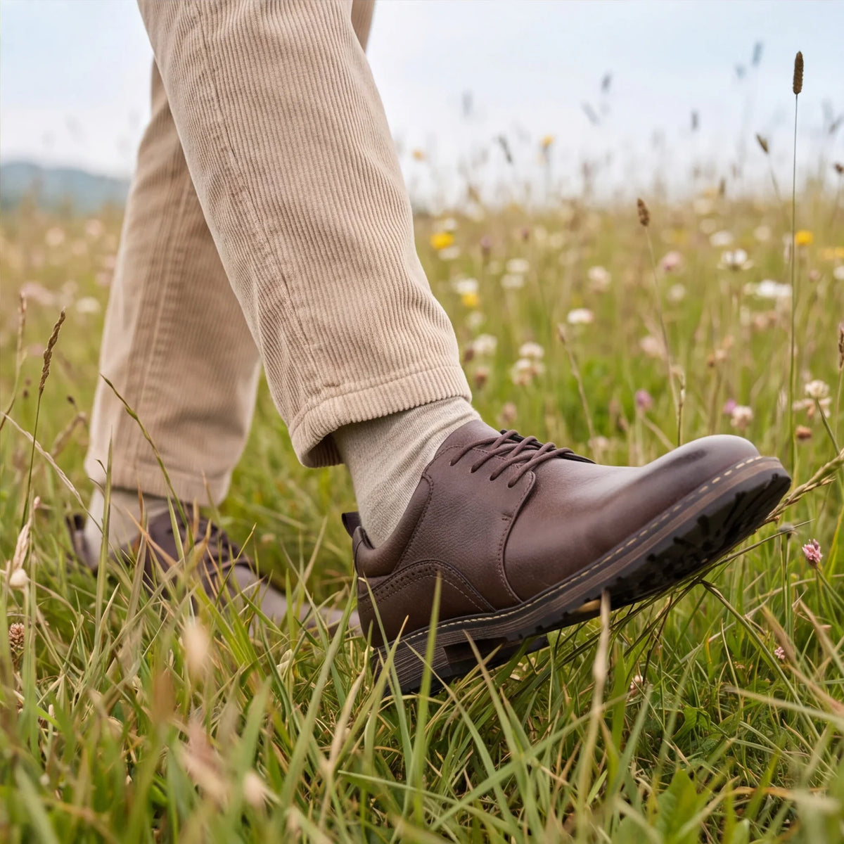 Brown lace-up derby shoes with a round toe, worn with beige corduroy pants in a grassy field.