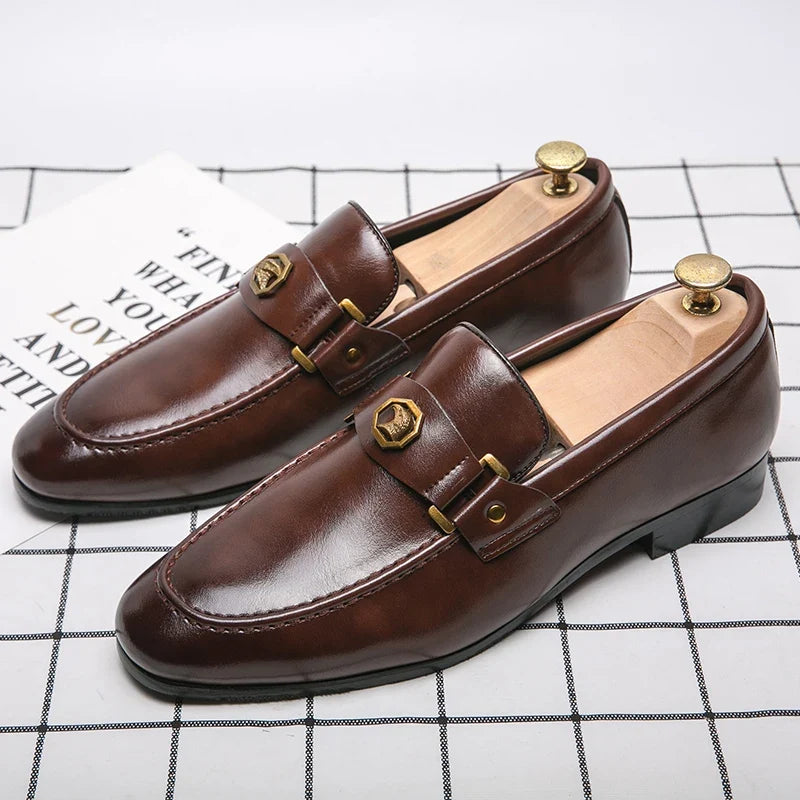Brown leather slip-on loafers with a metal buckle detail, featuring a round toe and stitched design.
