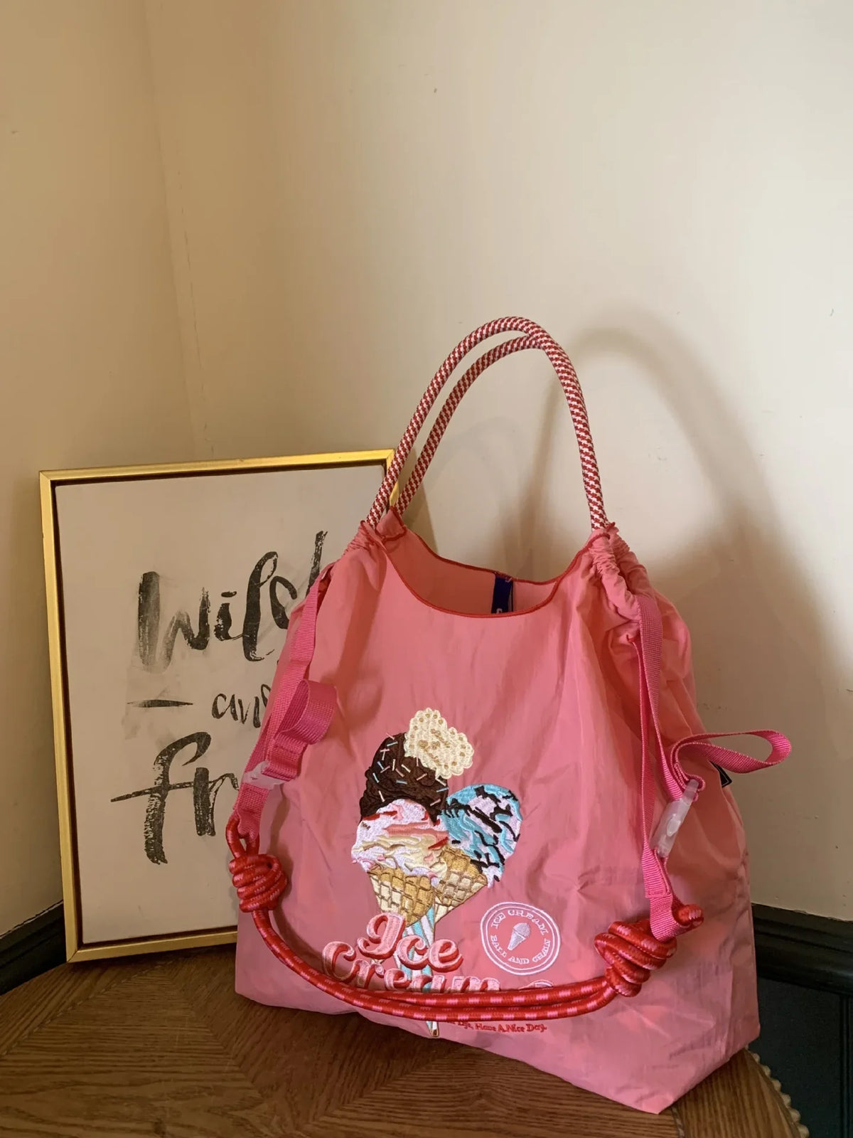 Light pink nylon tote bag with embroidered ice cream design, featuring a drawstring top and red patterned handles.