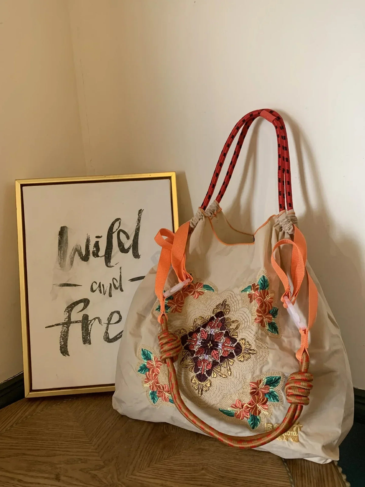 Lightweight, large-capacity tote bag with orange straps and floral embroidery on a cream nylon body, styled as a shoulder bag.