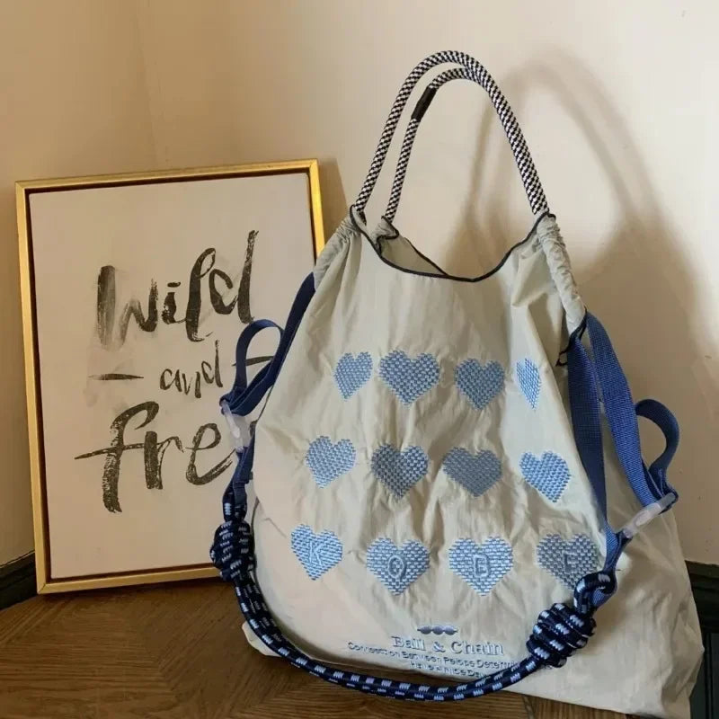 Light blue nylon tote bag with heart embroidery, casual style, featuring blue handles and a large capacity for storage.