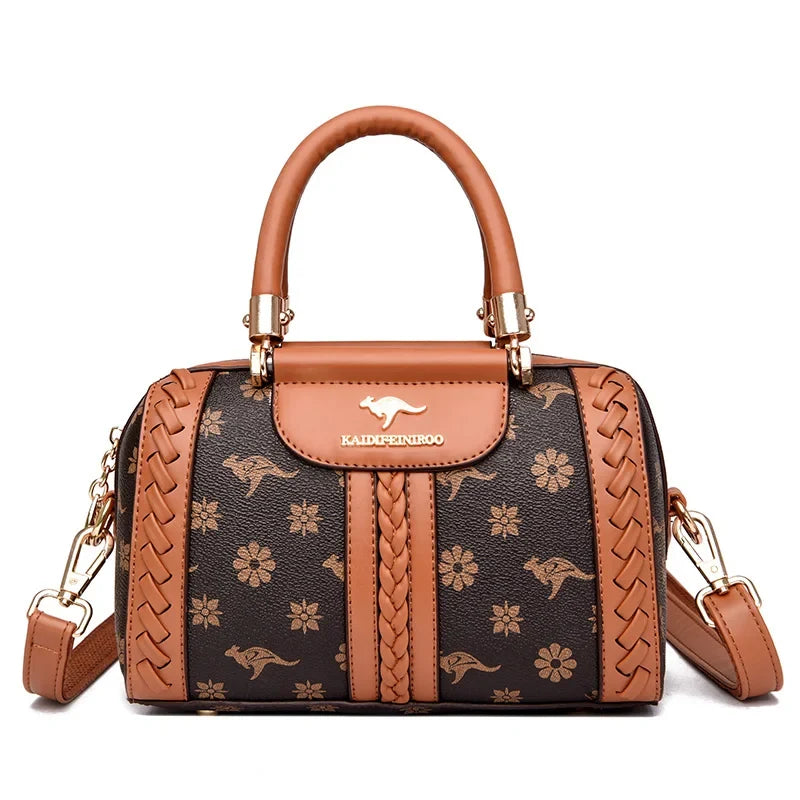 Brown and black designer shoulder bag with floral patterns, braided detailing, and a gold logo. Adjustable strap included.