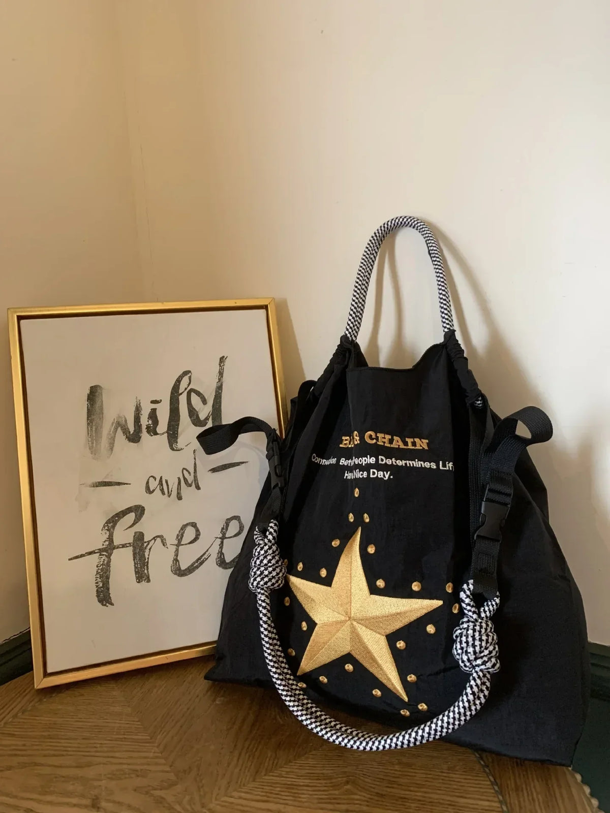 Large black nylon tote bag with a gold star design and striped handles, suitable for casual use or shopping.