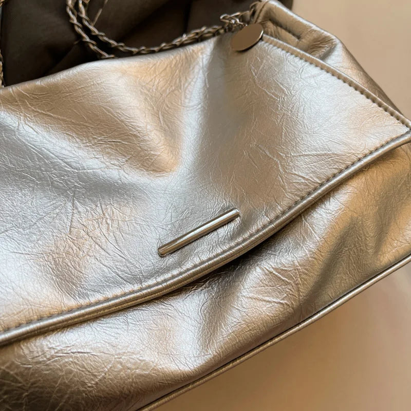 Silver shoulder bag made of soft leather with a flap closure and chain strap. Features a sleek, casual design.