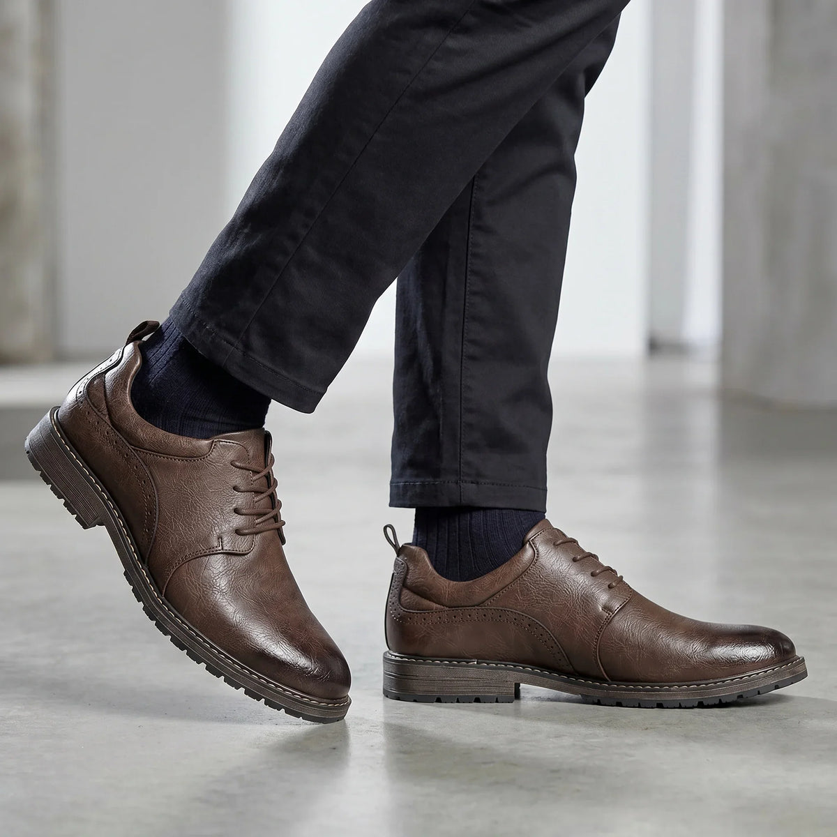 Brown lace-up derby shoes with a rubber sole, worn with dark pants and navy socks, showcasing a sleek and casual style.