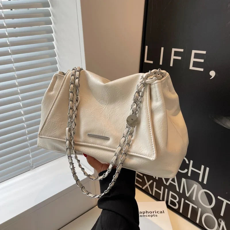 Silver shoulder bag featuring a soft leather finish, chain straps, and a large capacity, held in a hand against a window.