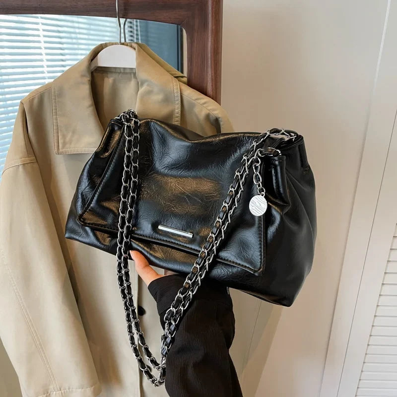Black soft leather shoulder bag with a silver chain strap, featuring a flap pocket and ample interior space.