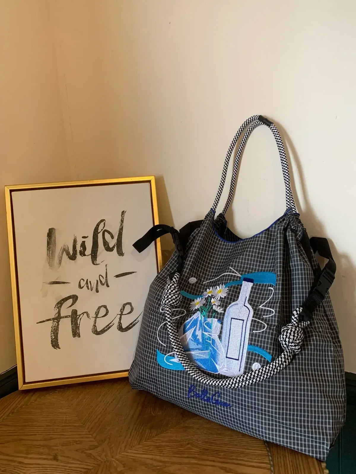 Large-capacity tote bag in black and gray checkered pattern with blue embroidered design and dual handles.