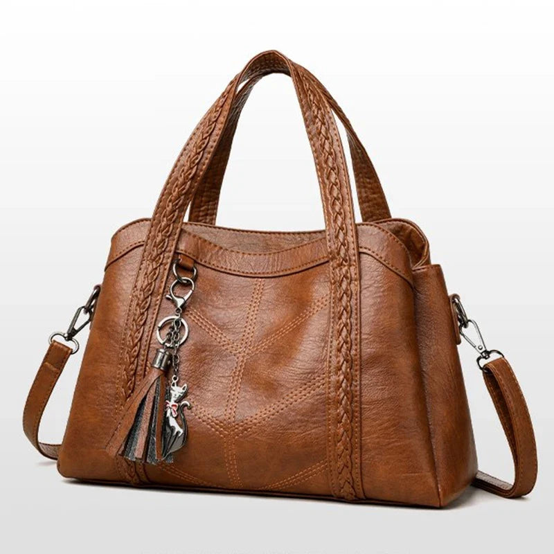 Brown leather tote bag with braided handles and a charm, featuring a zipper closure and spacious interior pockets.