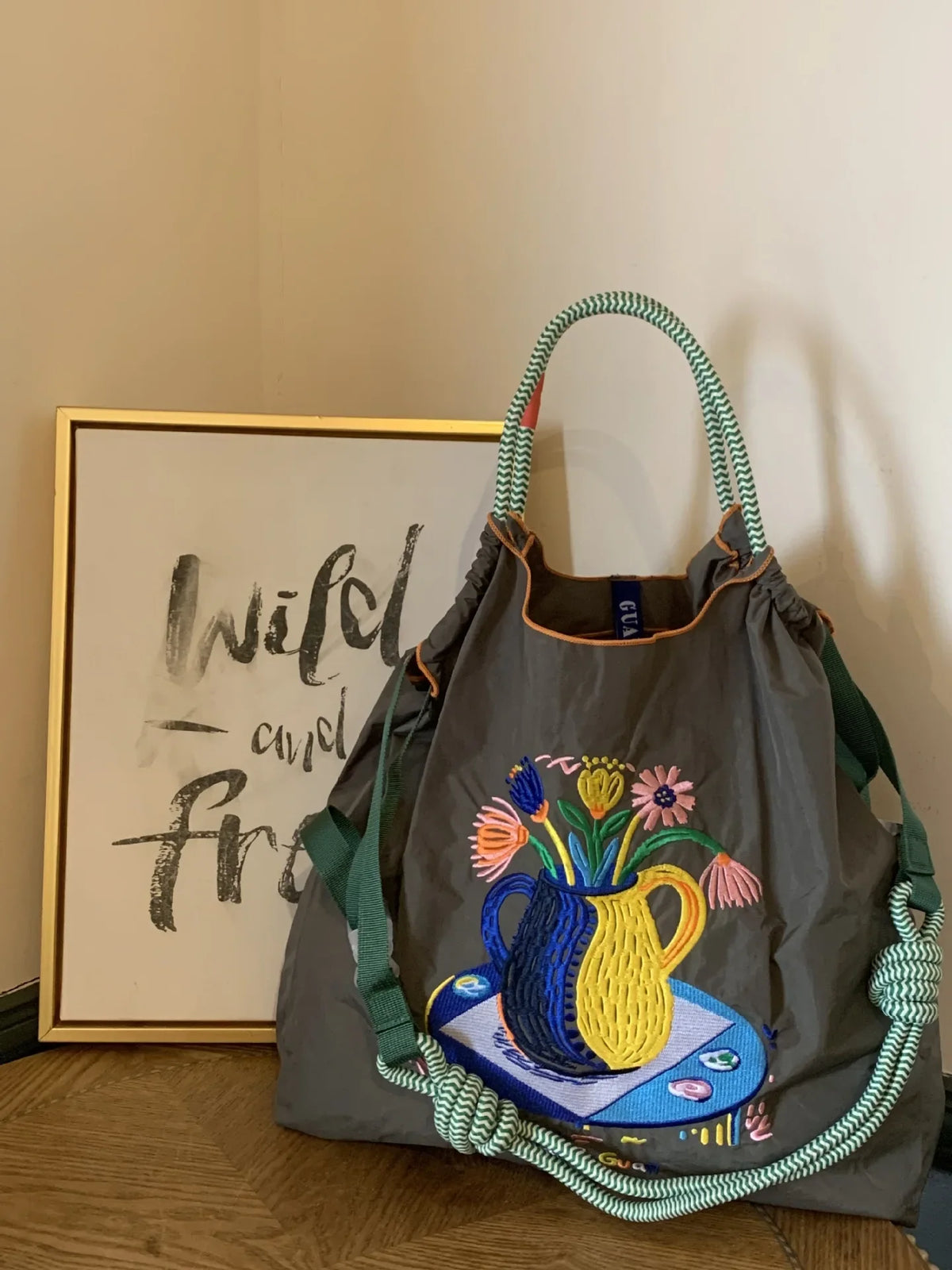 Large gray nylon tote bag with colorful floral embroidery, featuring a green rope handle and casual style.