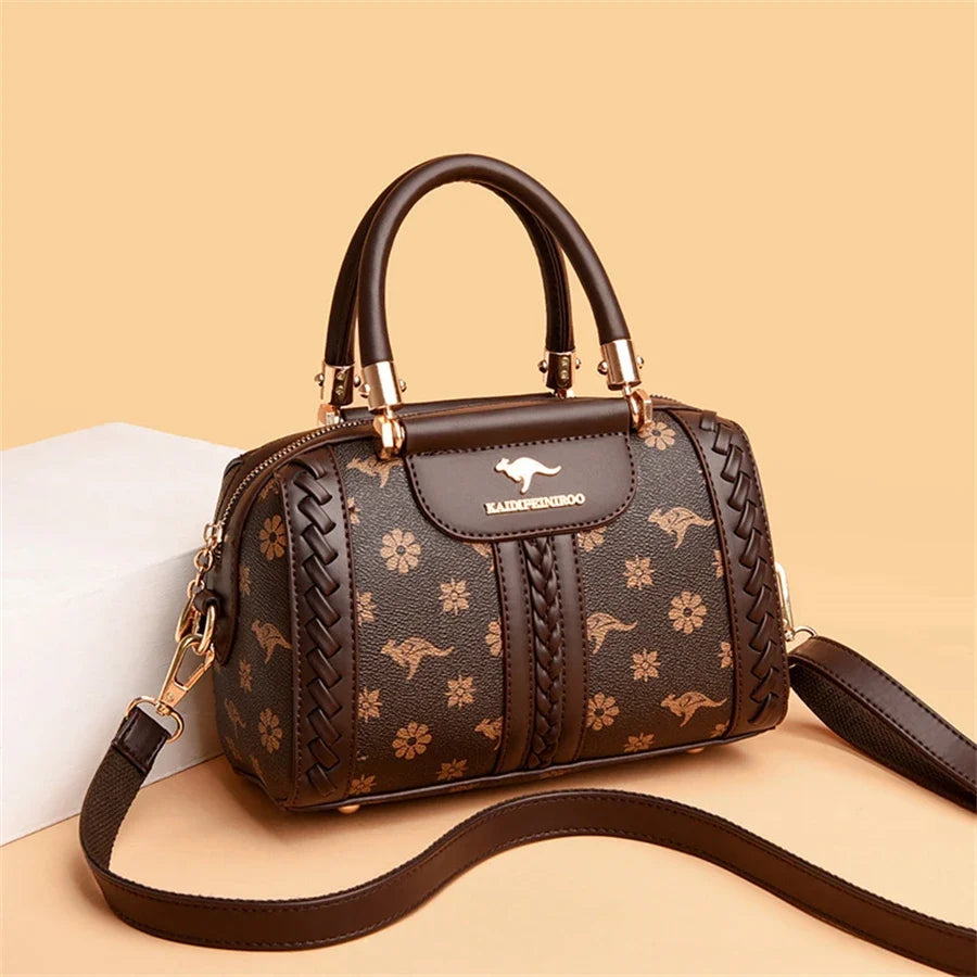 Brown luxury handbag with a woven texture, floral and animal print, featuring gold accents and an adjustable strap.