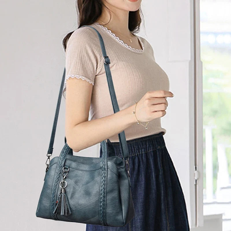 Blue leather handbag with braided details, worn casually over the shoulder, featuring a zip closure and tassel charm.