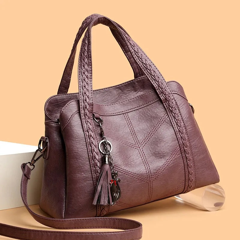 Braided leather shoulder bag in a muted purple tone; features a zipper closure, tassel charm, and sturdy handles.