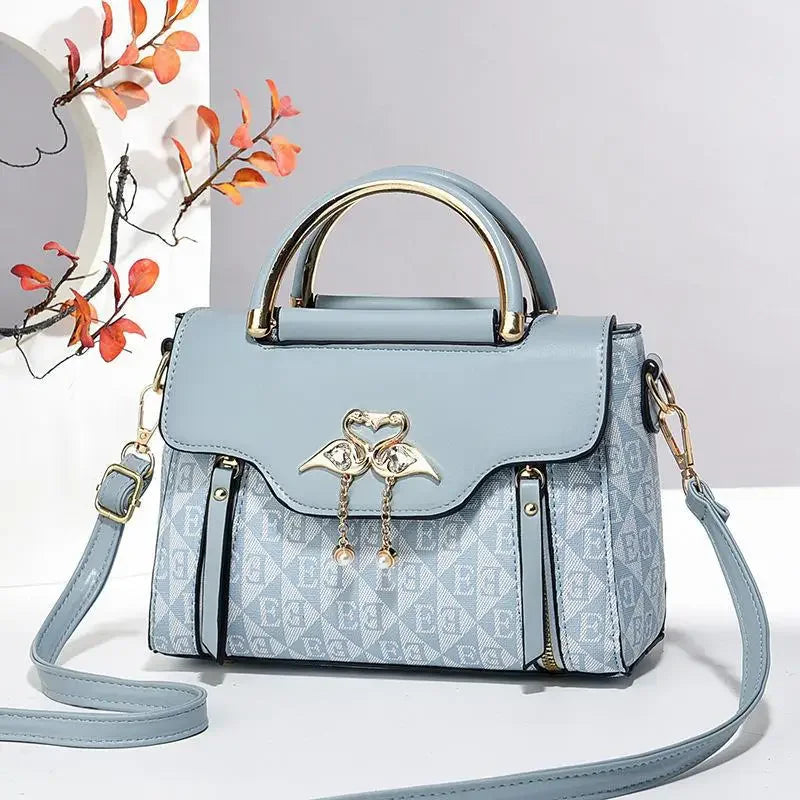 Light blue handbag with a gold accent clasp, soft exterior, and detachable shoulder strap. Stylish rectangular design.