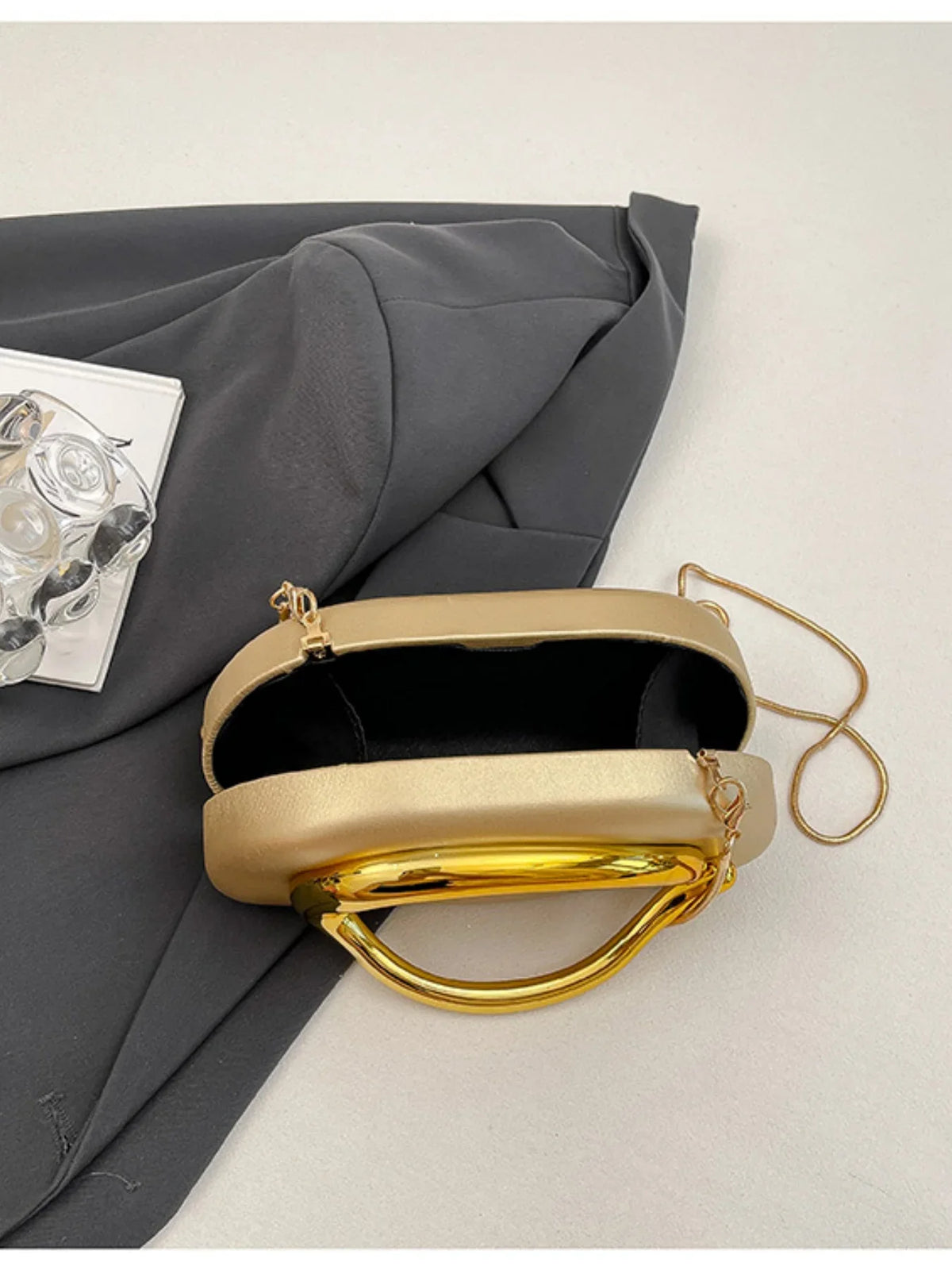 Elegant gold-accented handbag with a shell shape and solid beige PU exterior, featuring a black lining and detachable strap.
