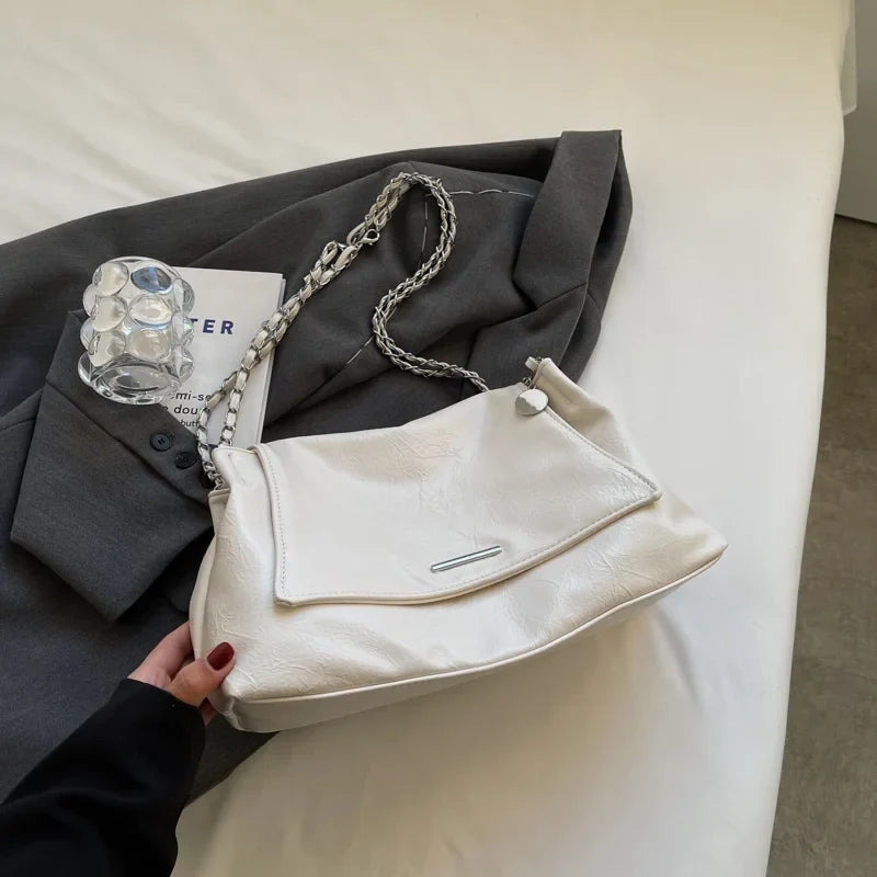 Soft white leather handbag with a silver chain strap, featuring a flap closure and heart-shaped charm.