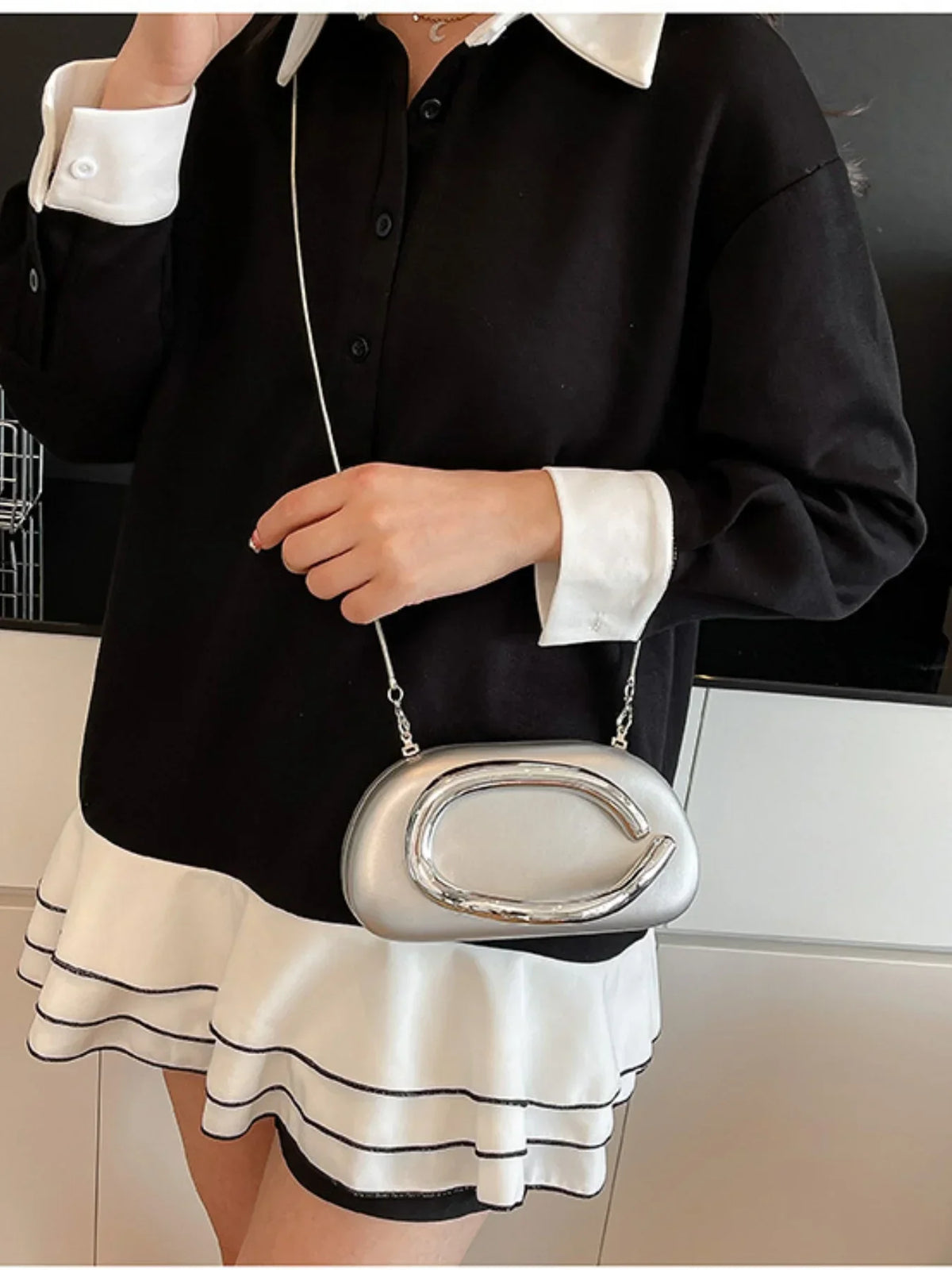 Ladies' elegant silver handbag with a shell shape, worn with a black and white shirt dress featuring a flared hem.