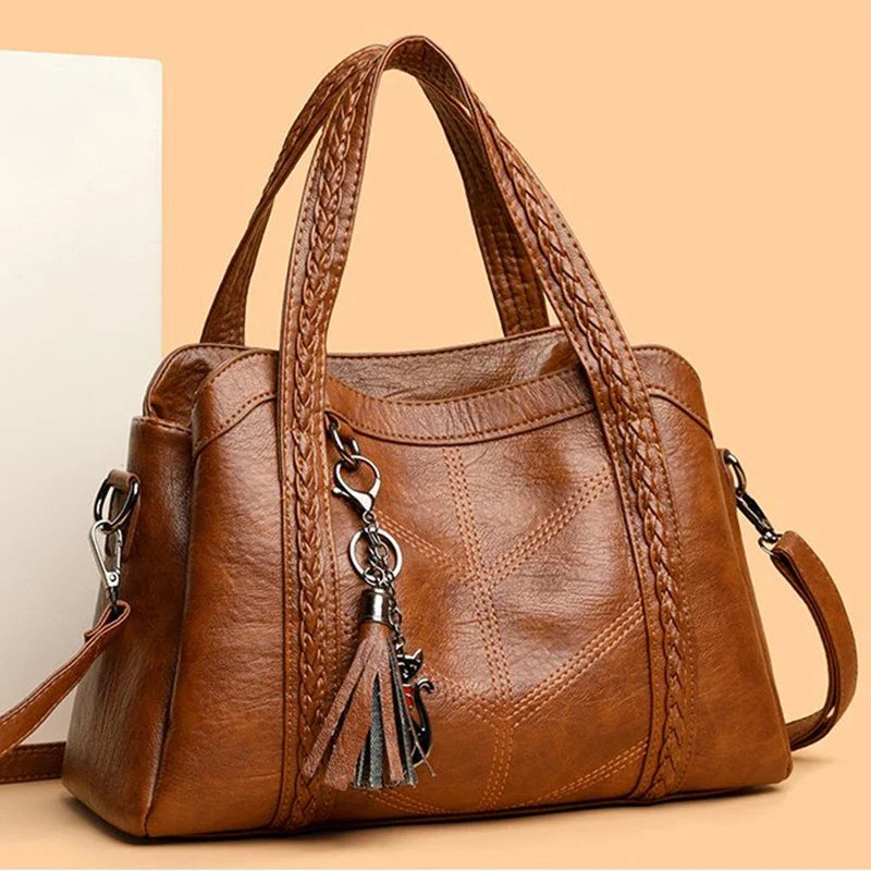Brown leather shoulder bag with braided handles and a decorative tassel. Features a soft texture and solid pattern.